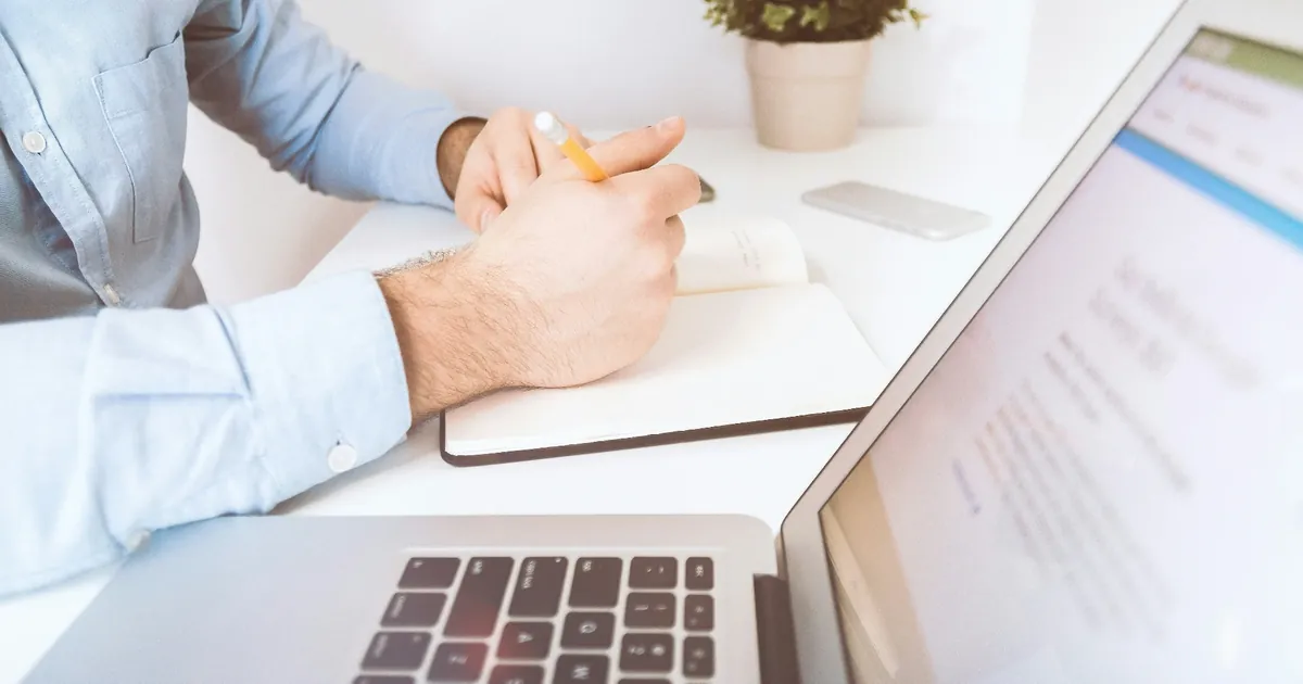 Indépendant en train de prendre des notes à son bureau à côté d'un ordinateur portable