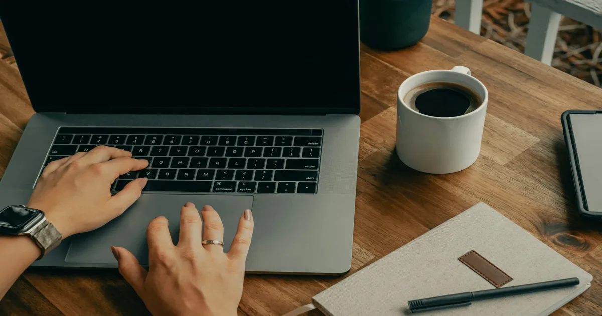 Indépendante en train de faire sa prospection digitale sur son ordinateur portable, avec un café et un carnet