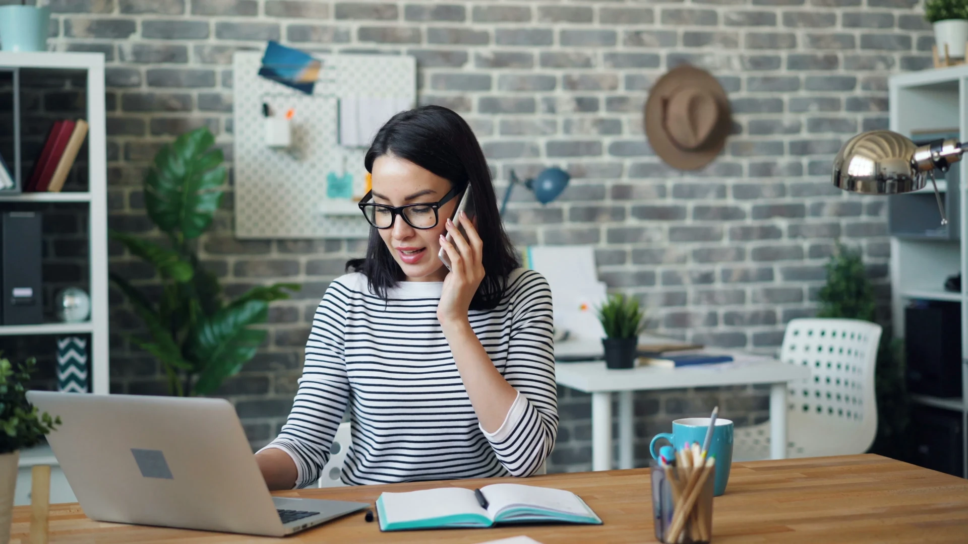 Indépendante au téléphone à son bureau, en train de relancer un prospect avec son ordinateur et son carnet de suivi